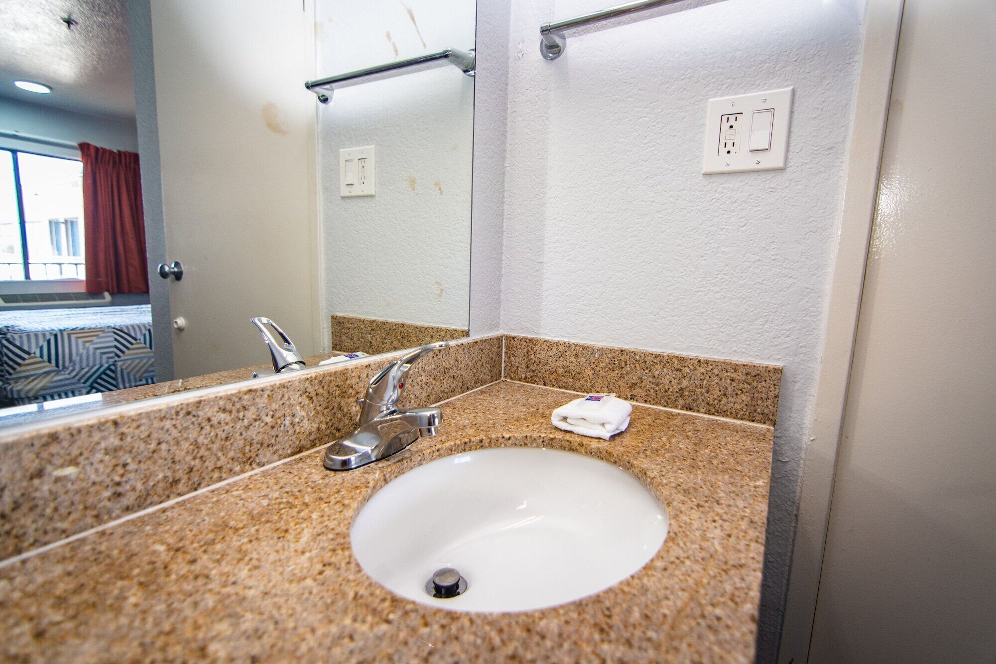 A bathroom with a granite countertop, a white sink, a mirror, and a towel rack.