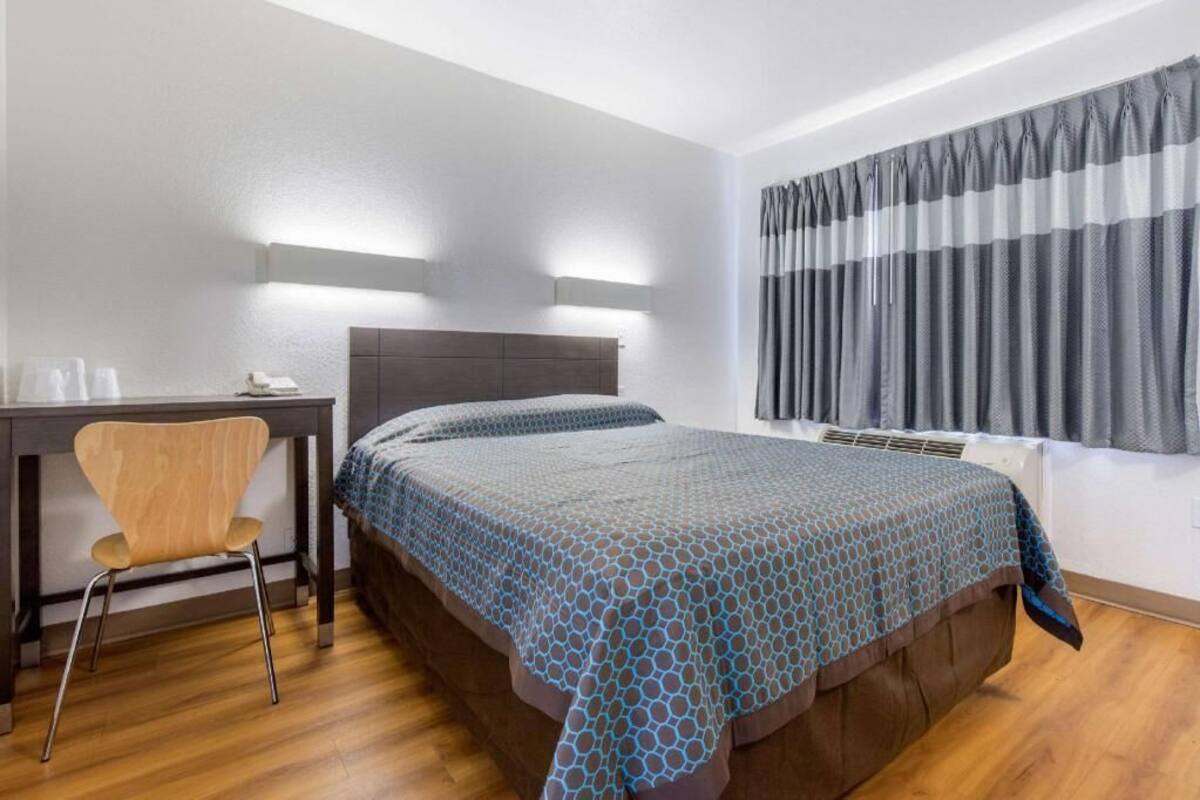 Ein Hotelzimmer mit einem Bett, einem Schreibtisch, einem Stuhl und einem Fenster mit Vorhängen.