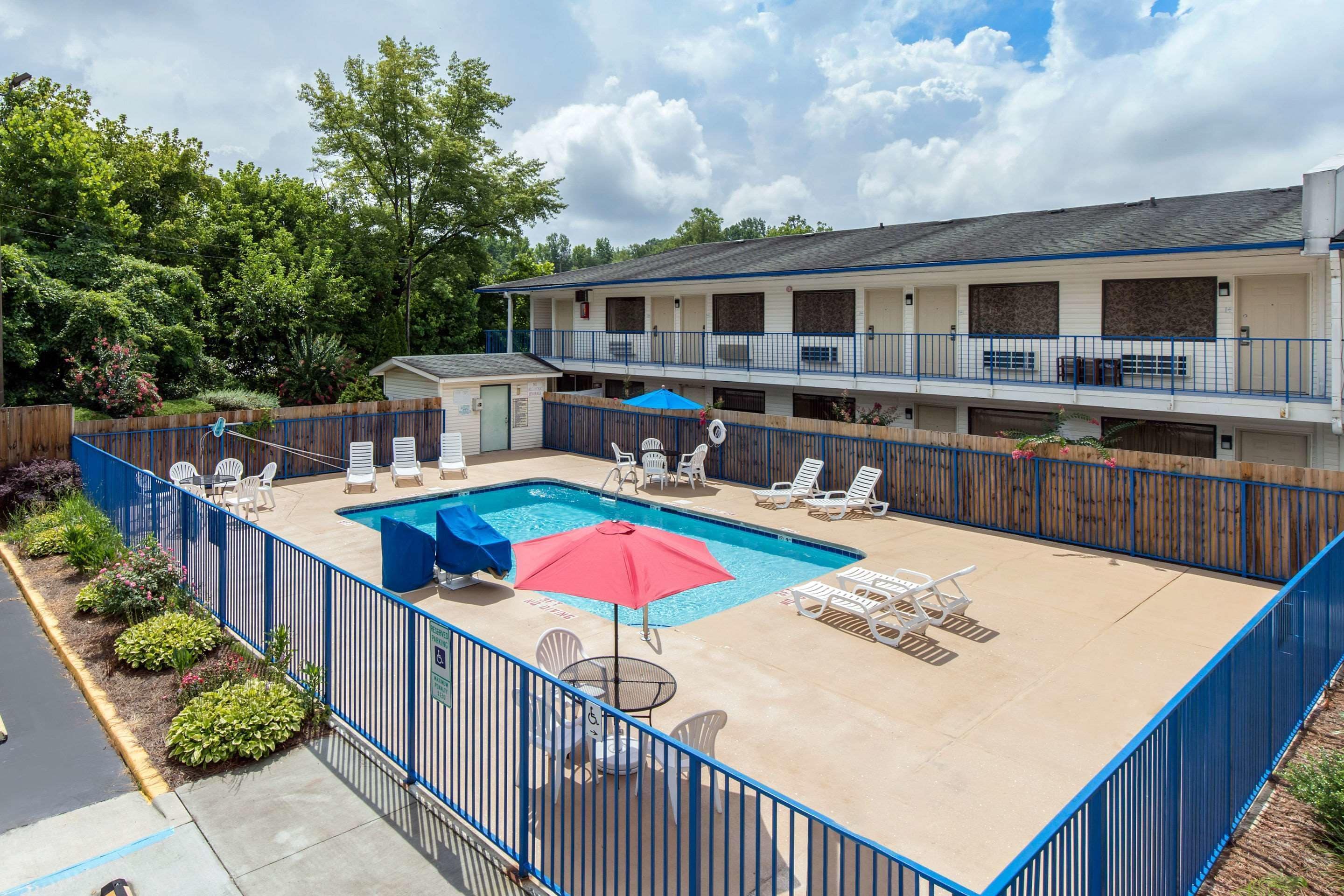 A motel with a swimming pool, outdoor seating, and a fenced patio area.