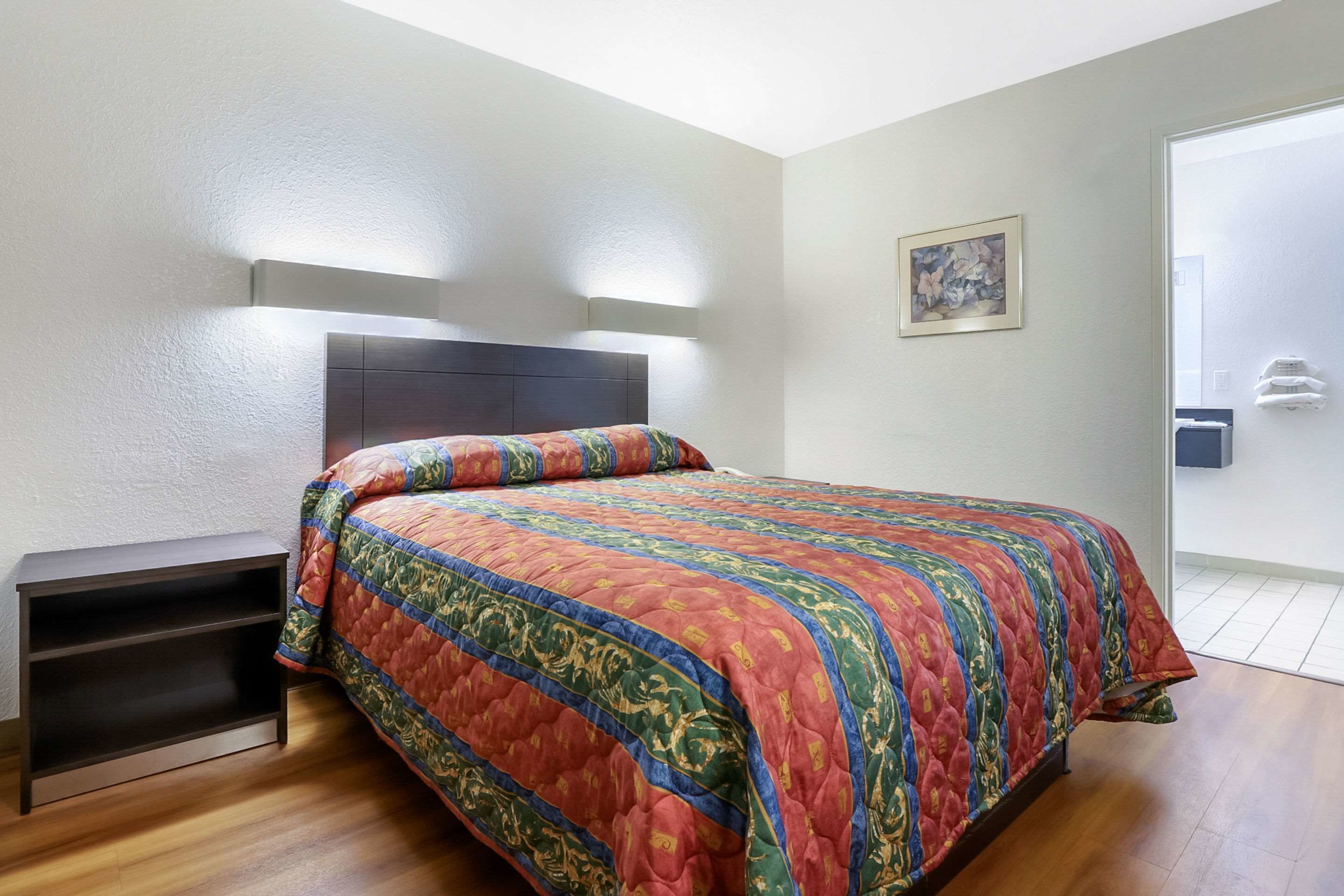 A bedroom with a bed, a nightstand, a wall-mounted light, and a door.