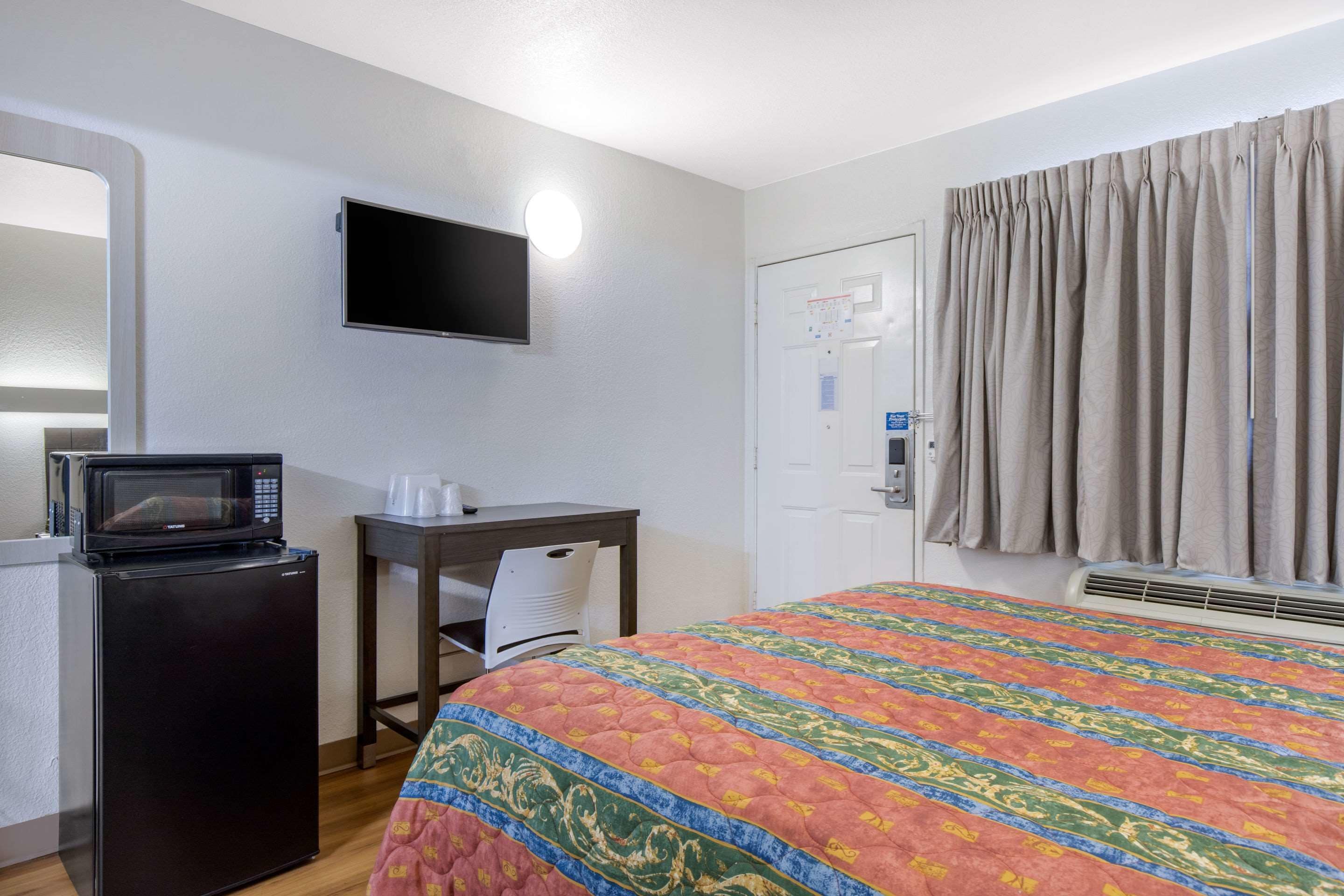 Habitación de hotel con cama, escritorio con microondas, televisión, puerta y ventana con cortinas.