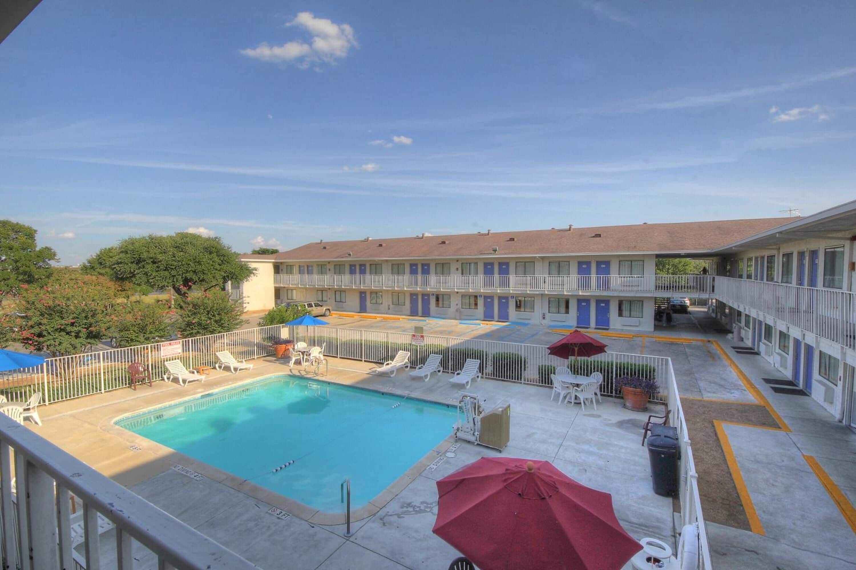 A hotel with a swimming pool, lounge chairs, and umbrellas.