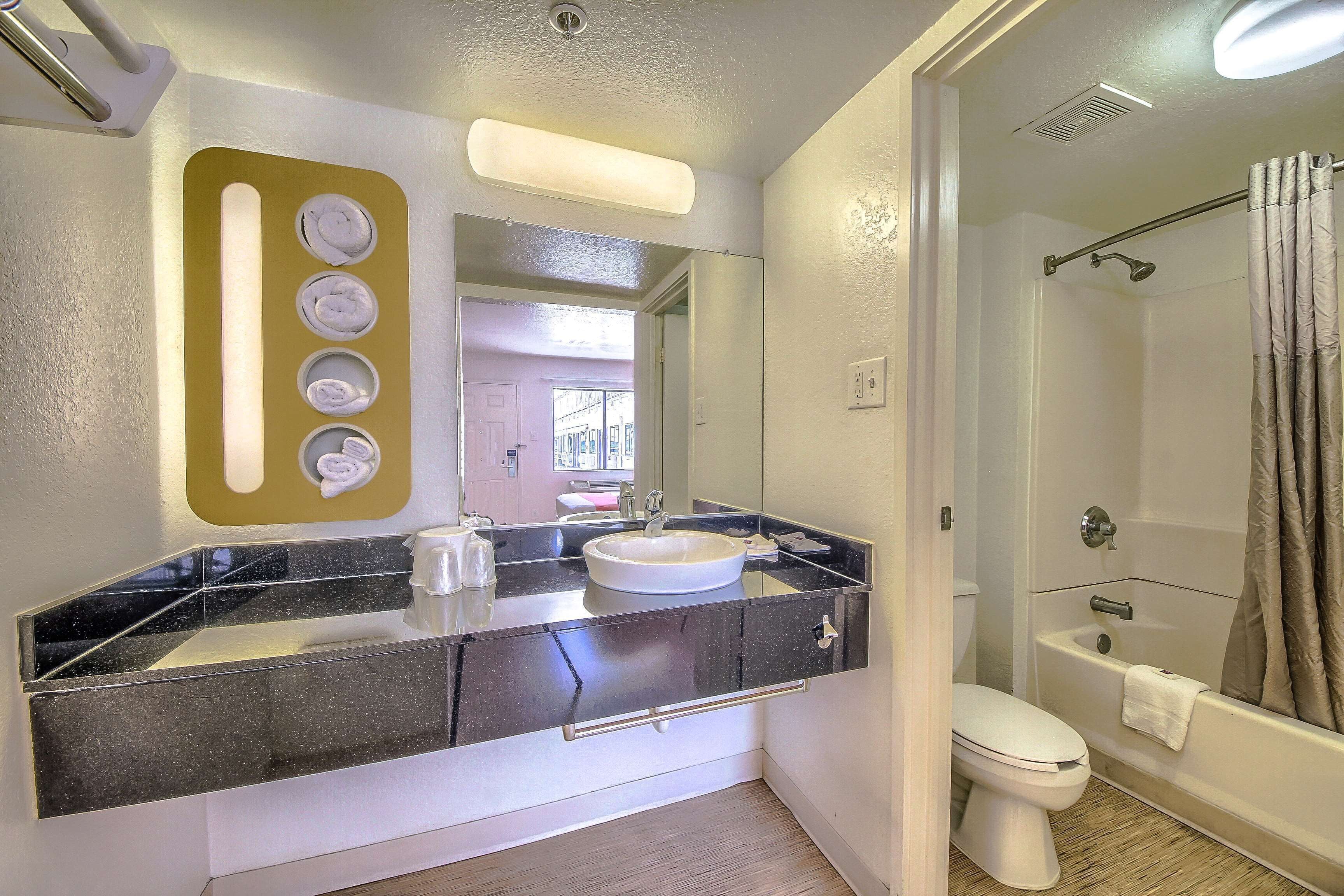 A bathroom with a black countertop, white sink, and a shower area.