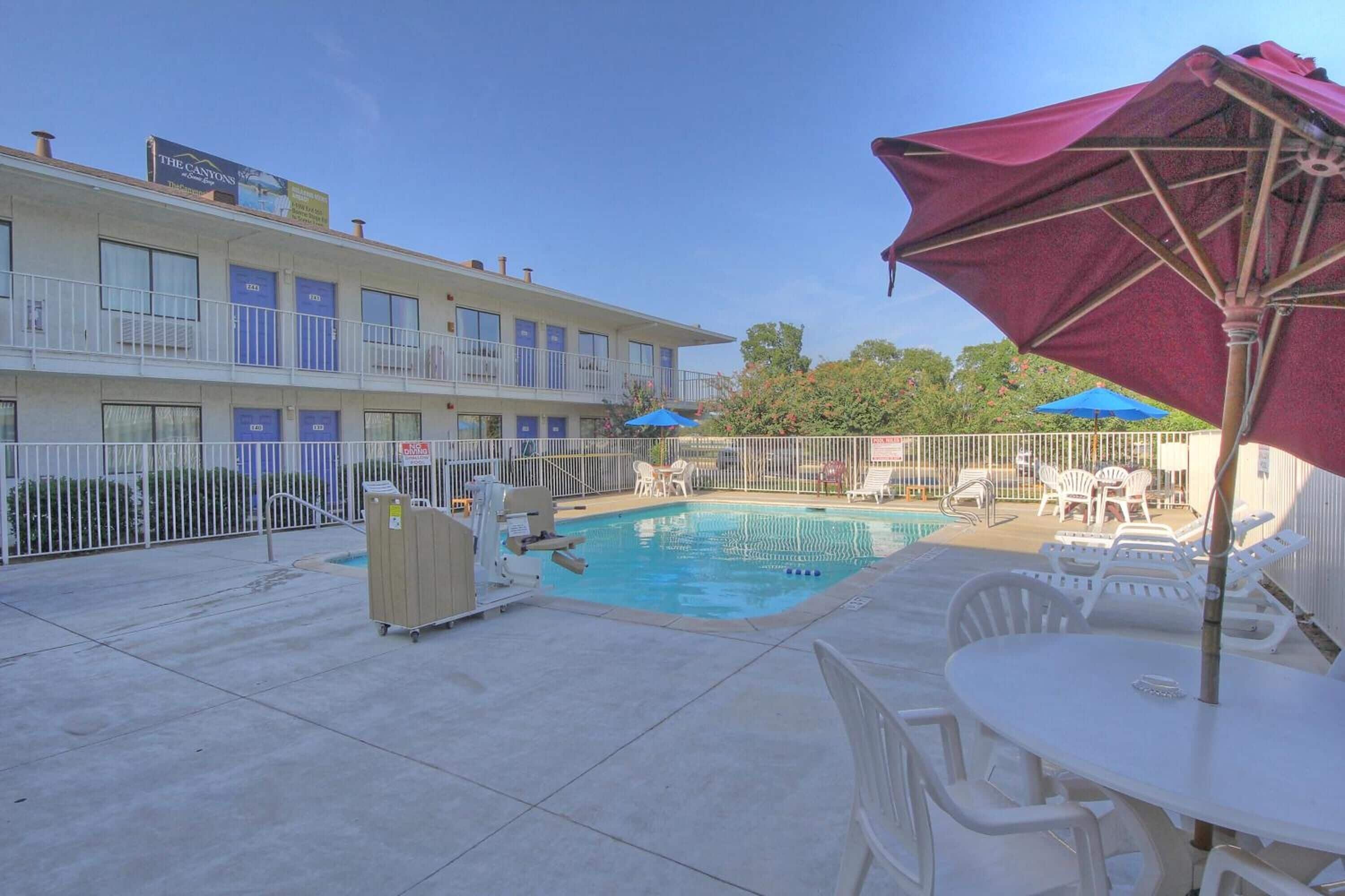 A hotel with a pool, outdoor seating, and a fenced area.