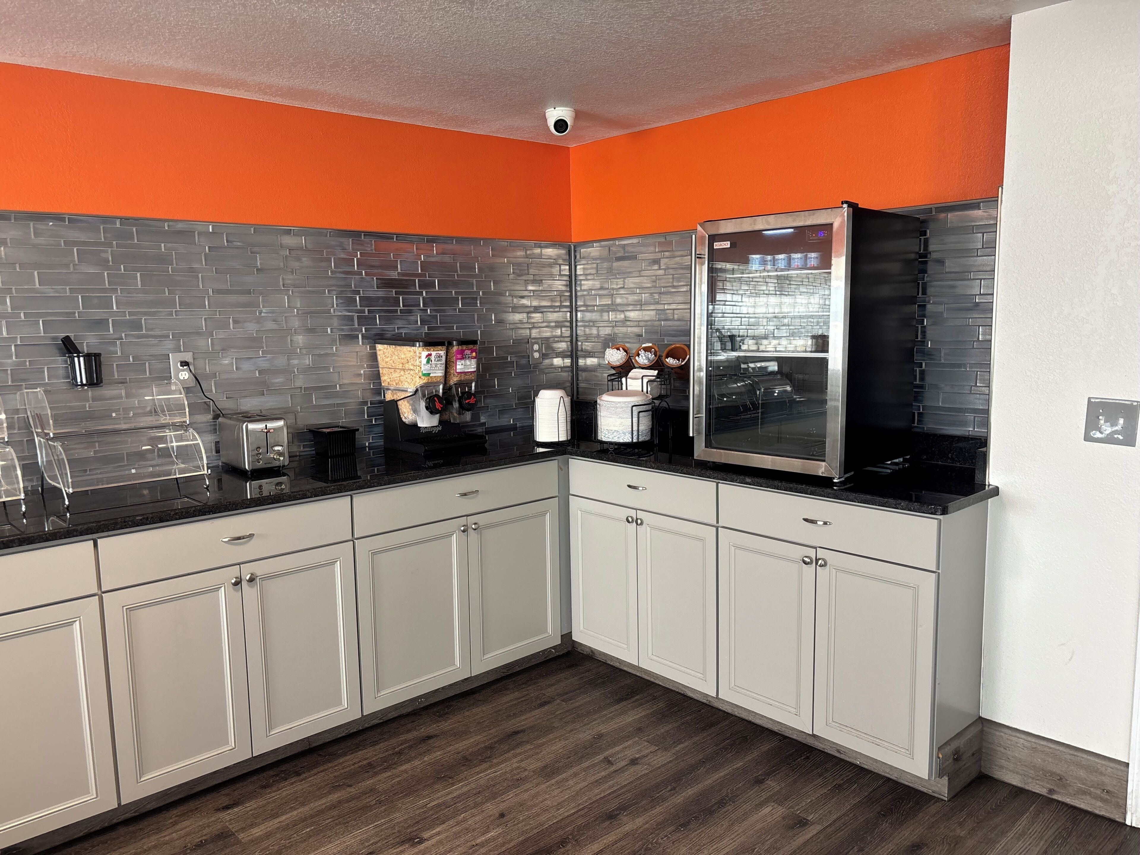 A kitchen with grey brick backsplash, white cabinets, and an orange accent wall.