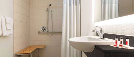 A shower with a bench, a sink with a mirror, and toiletries on the counter.