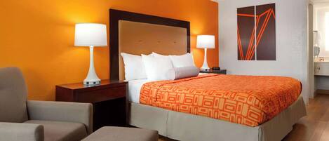 Habitación de hotel con una cama grande, dos mesitas de noche, una silla y una pared decorada con arte geométrico.