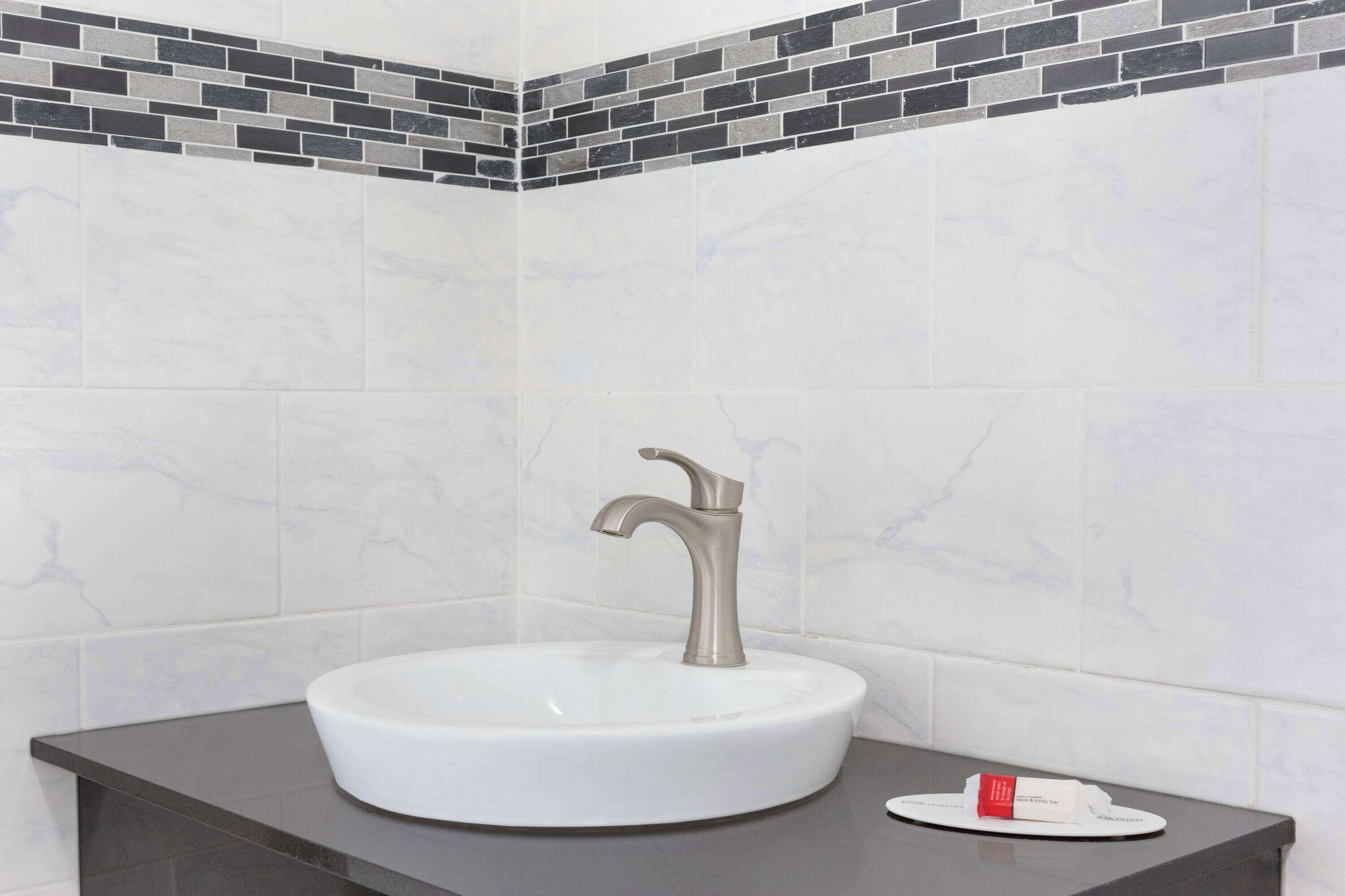 A bathroom with a white sink, a modern faucet, and a dark countertop.