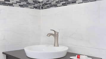 Un baño con un lavamanos blanco, un grifo moderno y una encimera oscura.