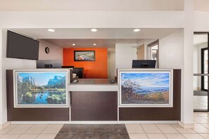 A reception desk with two framed landscape paintings, a clock, and a television on the wall.