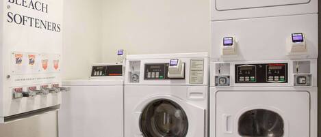 A laundry facility with multiple washing machines and a sign listing soap, bleach, and softeners.