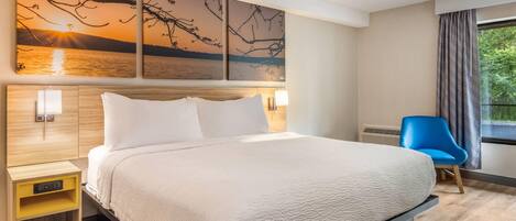 A hotel room with a bed, bedside tables, a lamp, a chair, and a large window with curtains.