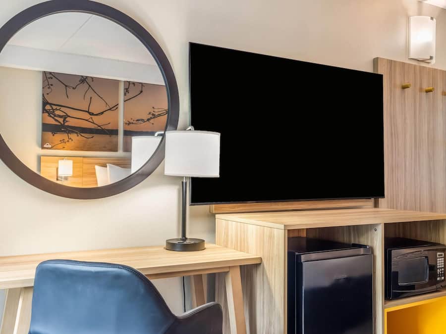 A hotel room with a desk, chair, television, microwave, and a mirror.