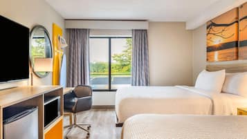 A hotel room with a bed, a desk with a TV, a chair, and a window with curtains.