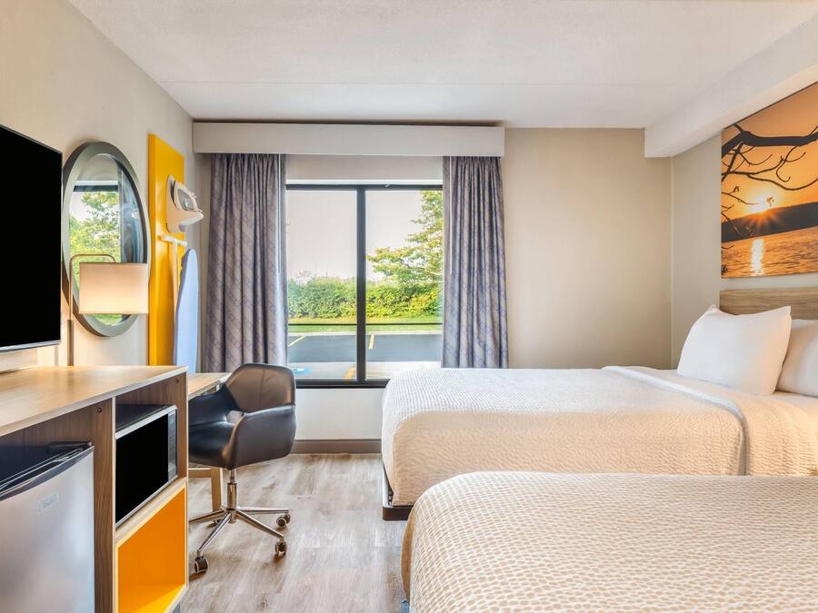 A hotel room with a bed, a desk with a TV, a chair, and a window with curtains.