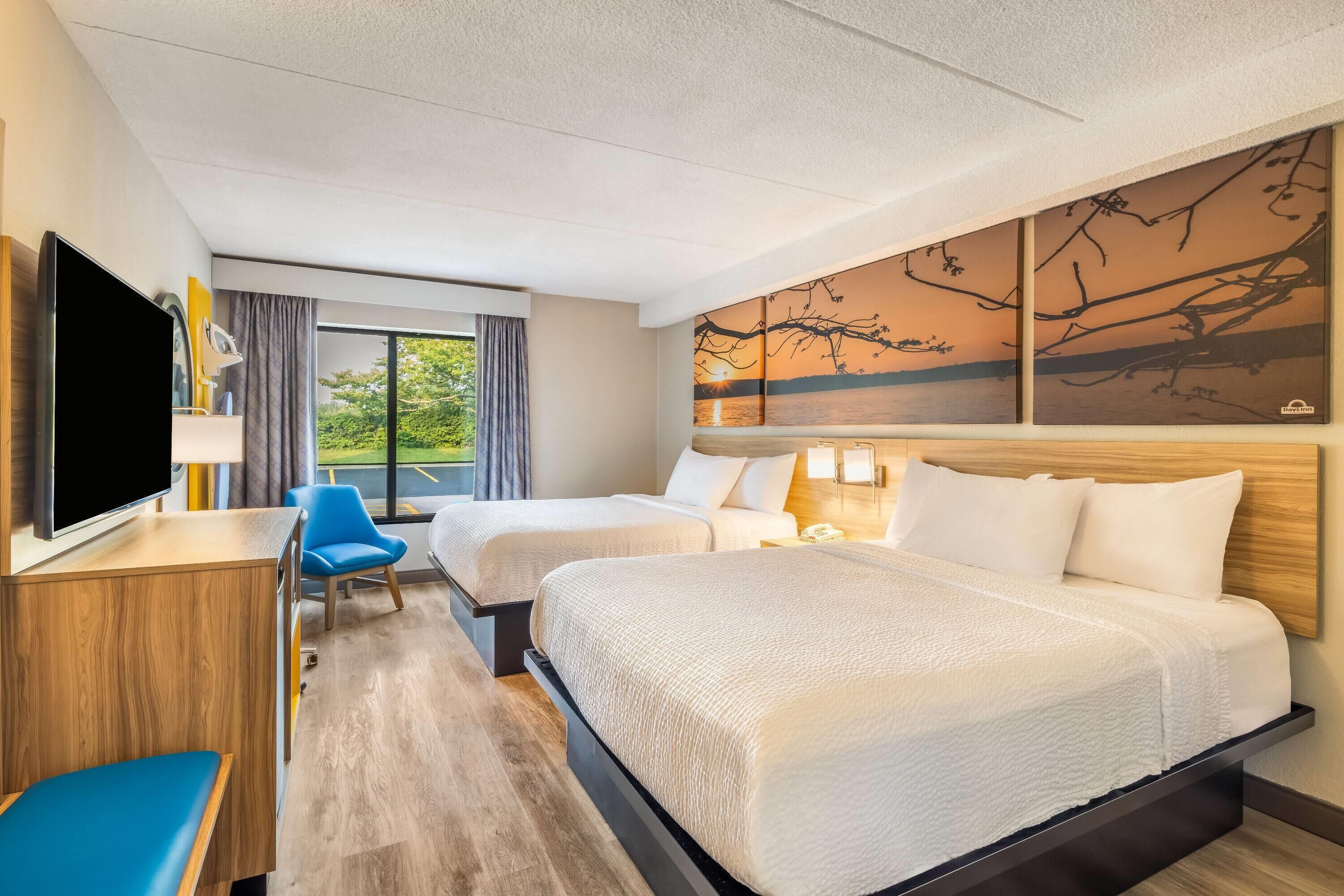 A hotel room with two beds, a TV, a desk, a chair, and a painting on the wall.