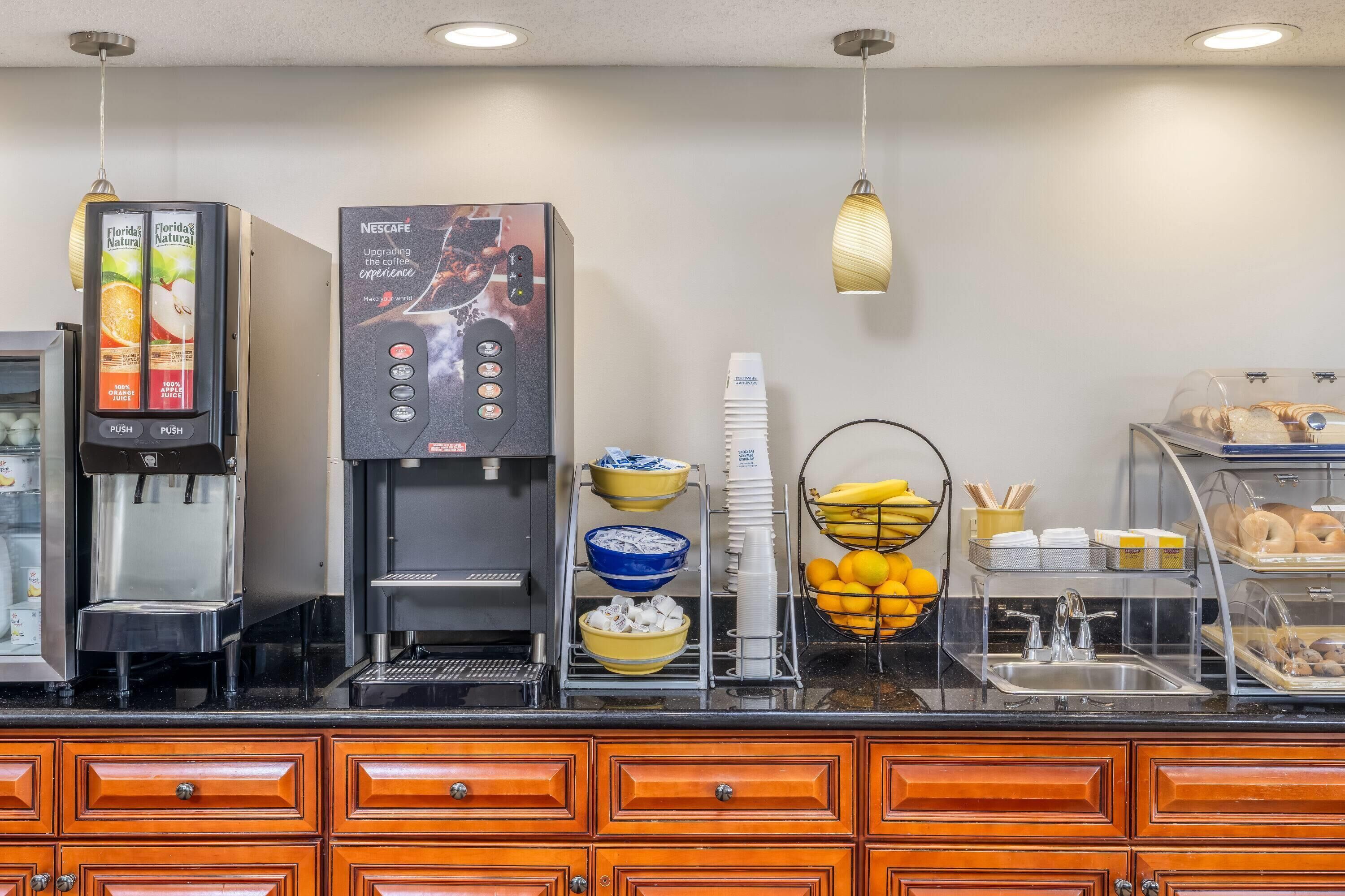 A coffee station with a Nescafe machine, a juice dispenser, and a variety of breakfast items like bananas, oranges, and pastries.