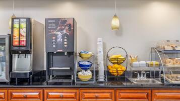 A coffee station with a Nescafe machine, a juice dispenser, and a variety of breakfast items like bananas, oranges, and pastries.