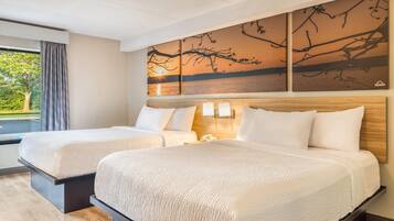 Habitación de hotel con dos camas, un ventanal con cortinas y una obra de arte en la pared que muestra ramas de árboles.