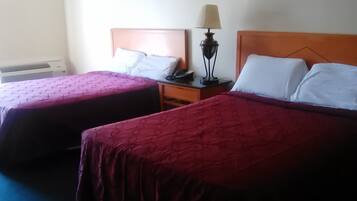 Two single beds with wooden headboards, a bedside table with a lamp, and a wall-mounted air conditioner.