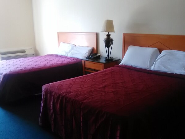 Two single beds with wooden headboards, a bedside table with a lamp, and a wall-mounted air conditioner. - Americas Best Value Inn Horseheads (Horseheads)