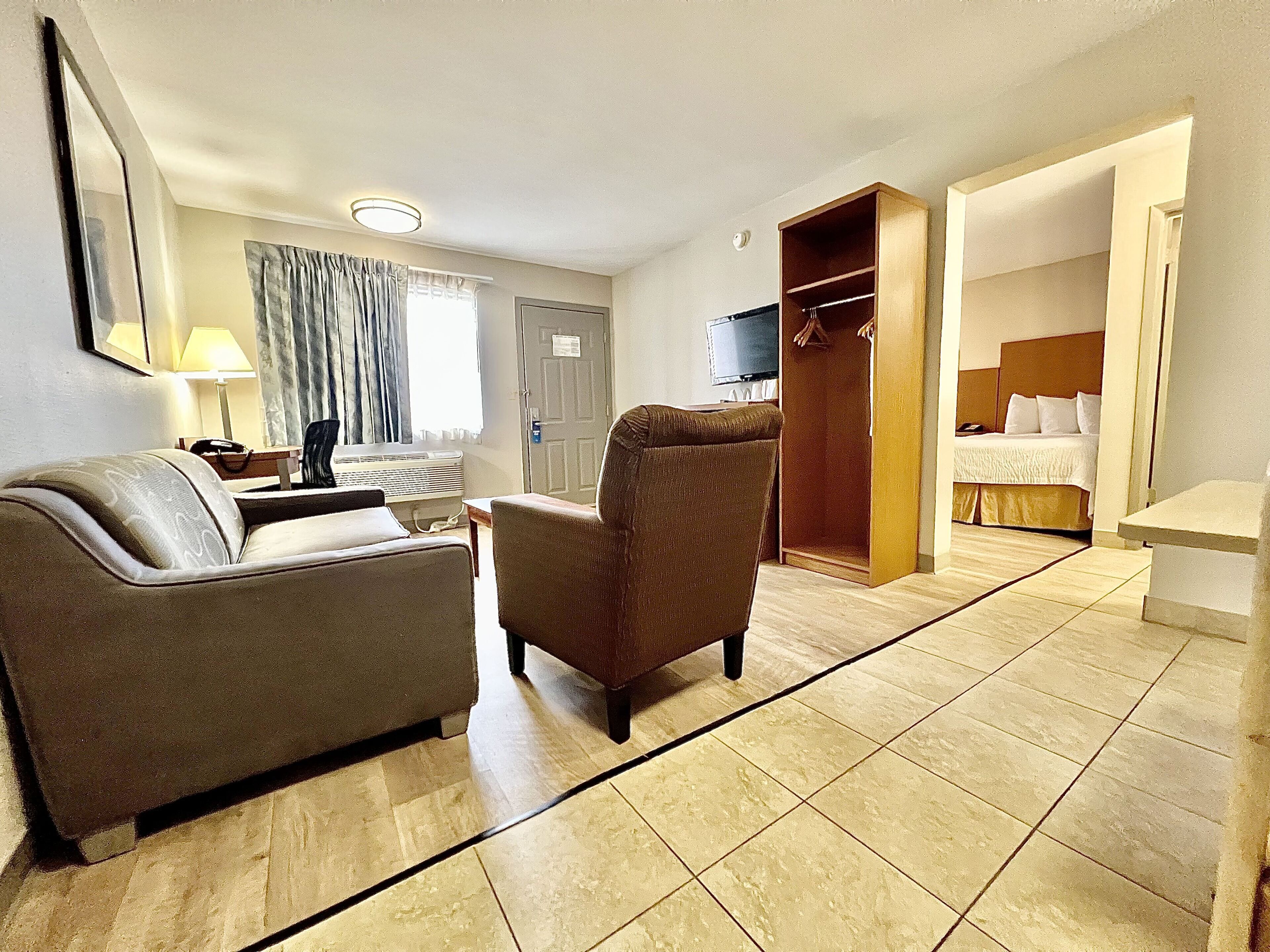 A hotel room with a sofa, armchair, bed, TV, and a wooden wardrobe.