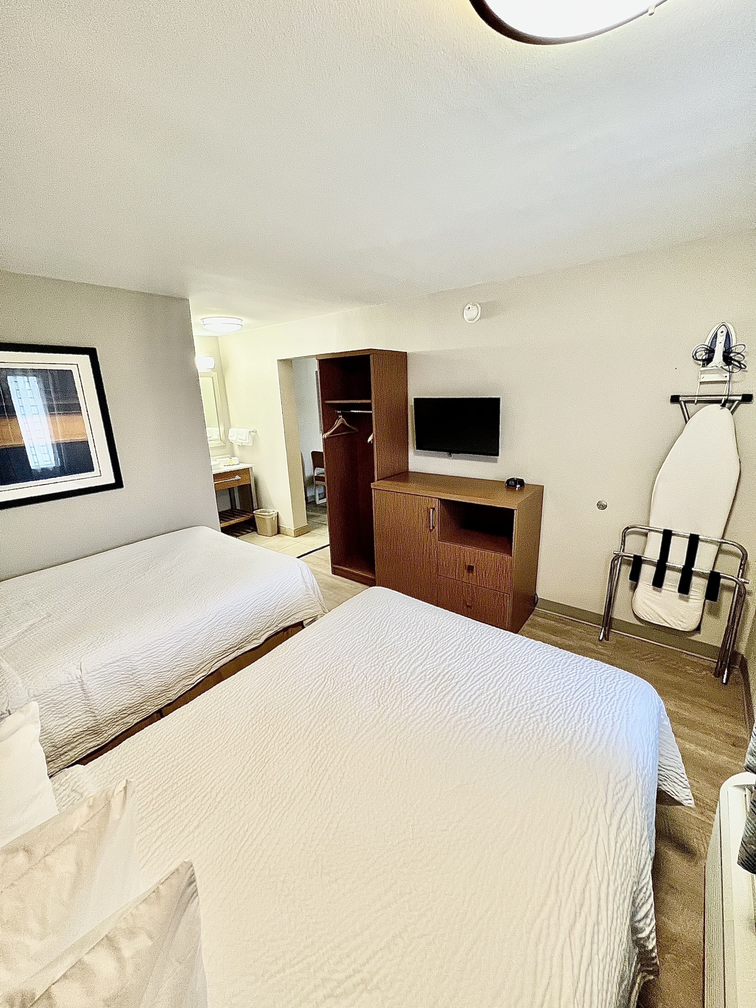 Habitació d'hotel amb dos llits, una televisió, una taula de planxa i un armari.