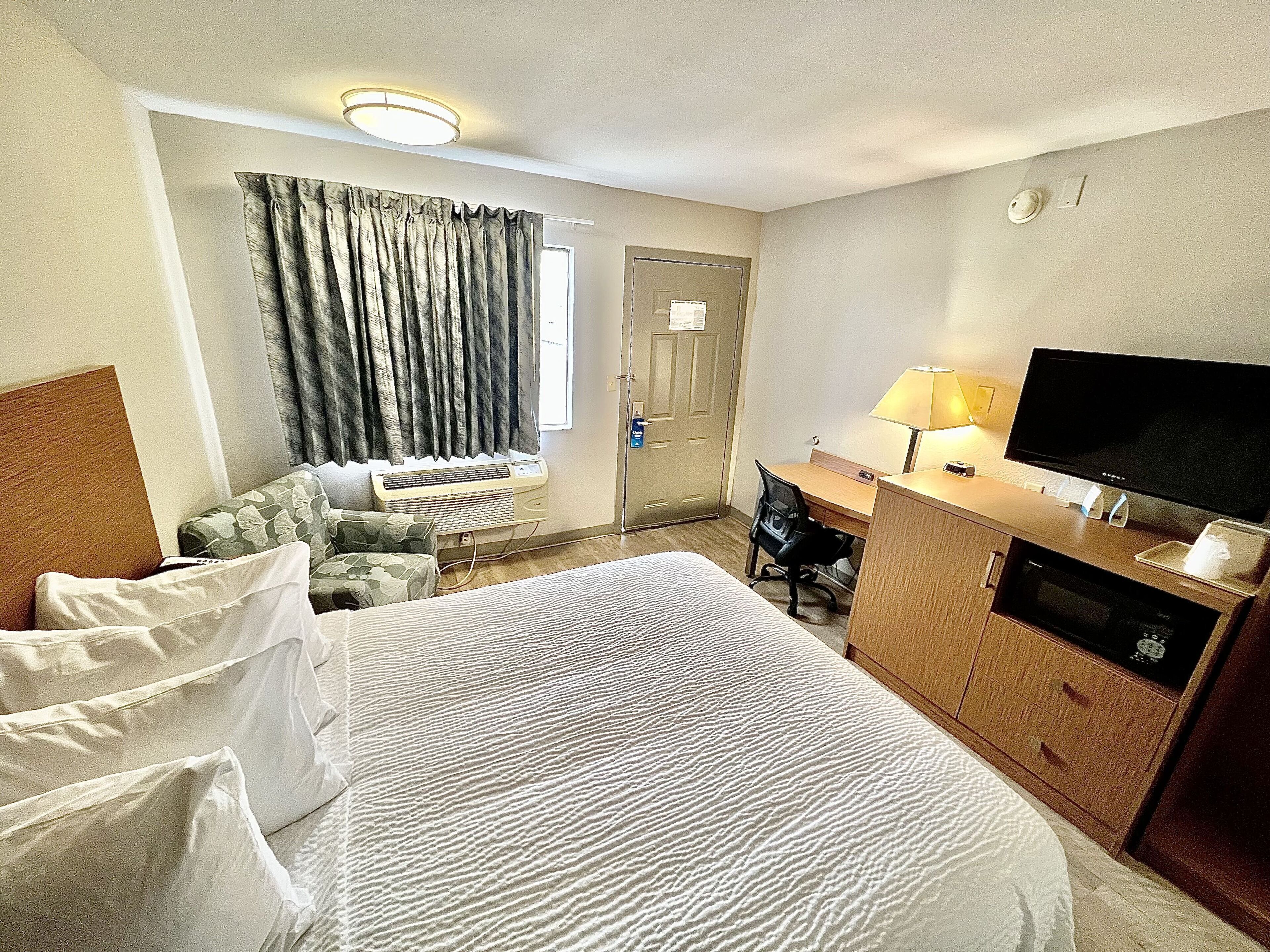 Habitación de hotel con cama, escritorio, silla, televisión y ventana con cortinas.