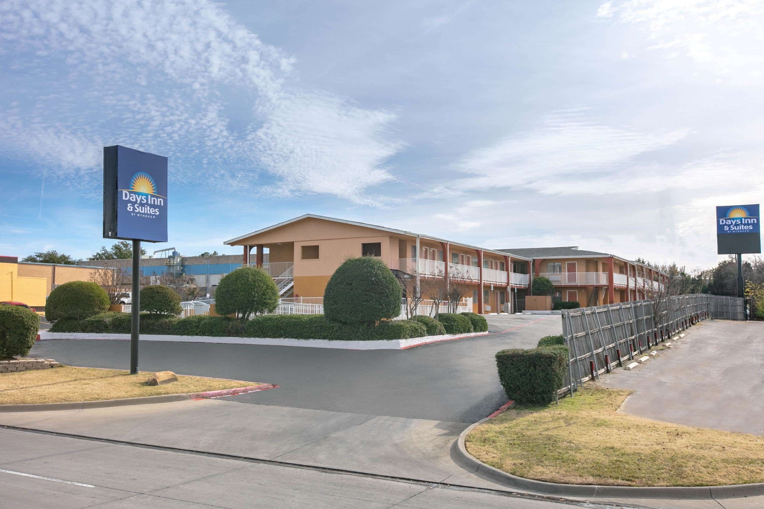 A Days Inn & Suites hotel with a modern design, featuring a central courtyard with neatly trimmed bushes and a fenced parking area.