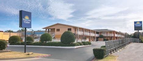 A Days Inn & Suites hotel with a modern design, featuring a central courtyard with neatly trimmed bushes and a fenced parking area.