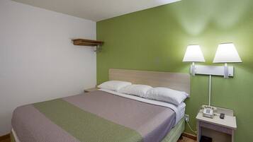 A hotel room with a bed, a nightstand with a lamp, and a green wall.