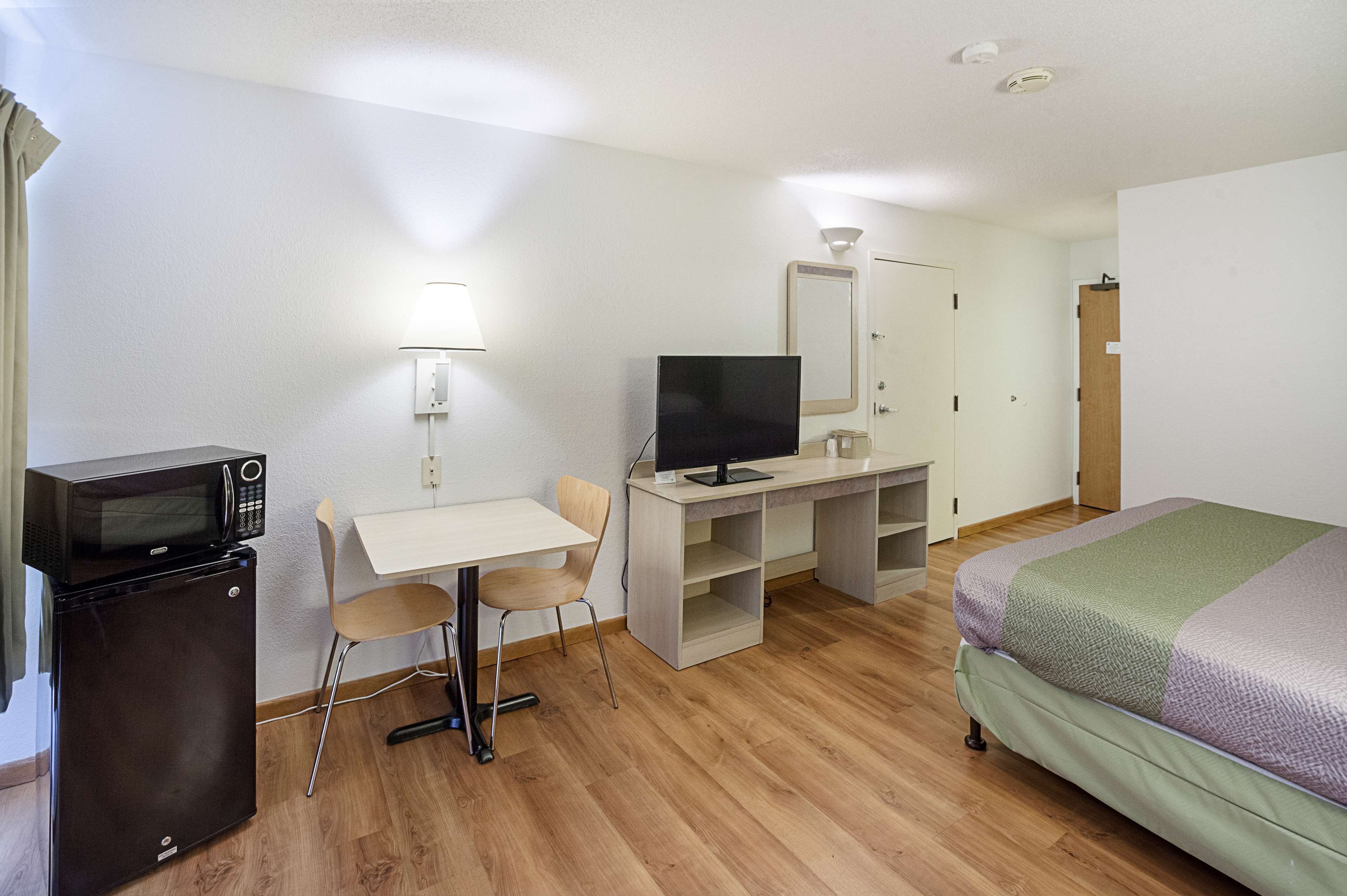 Een hotelkamer met een bed, een bureau met een computer en een televisie, een magnetron en een stoel.