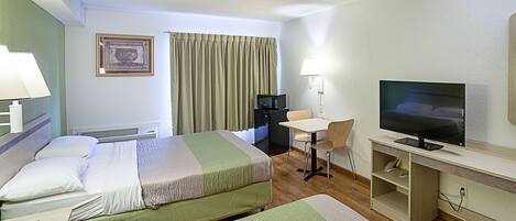 A hotel room with two beds, a desk with a chair, a television, and a lamp.