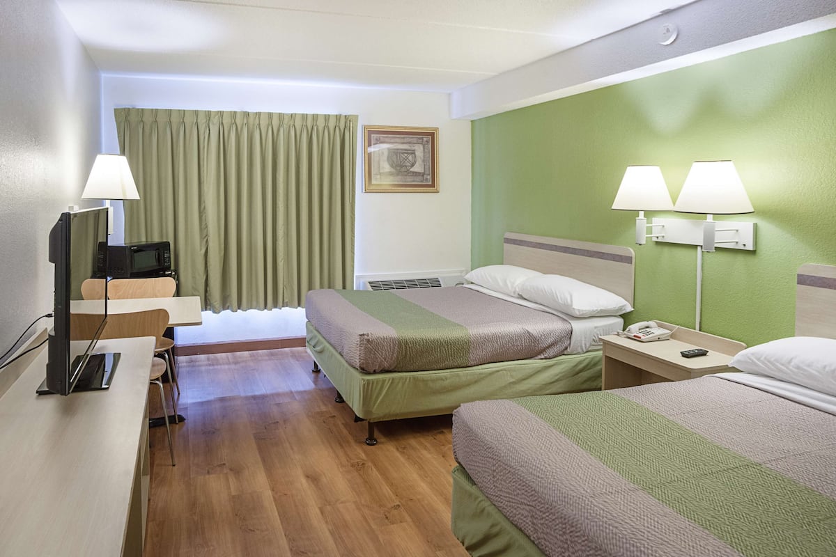 Habitación de hotel con dos camas, un escritorio con computadora, teléfono y televisor.