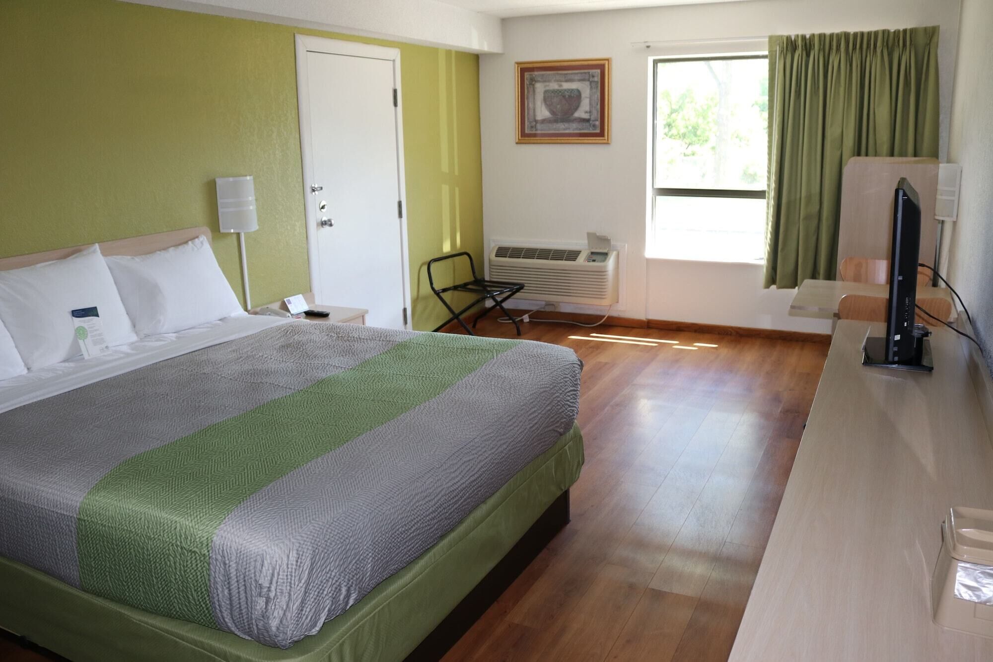 A hotel room with a bed, a desk, a chair, an air conditioning unit, and a window with curtains.
