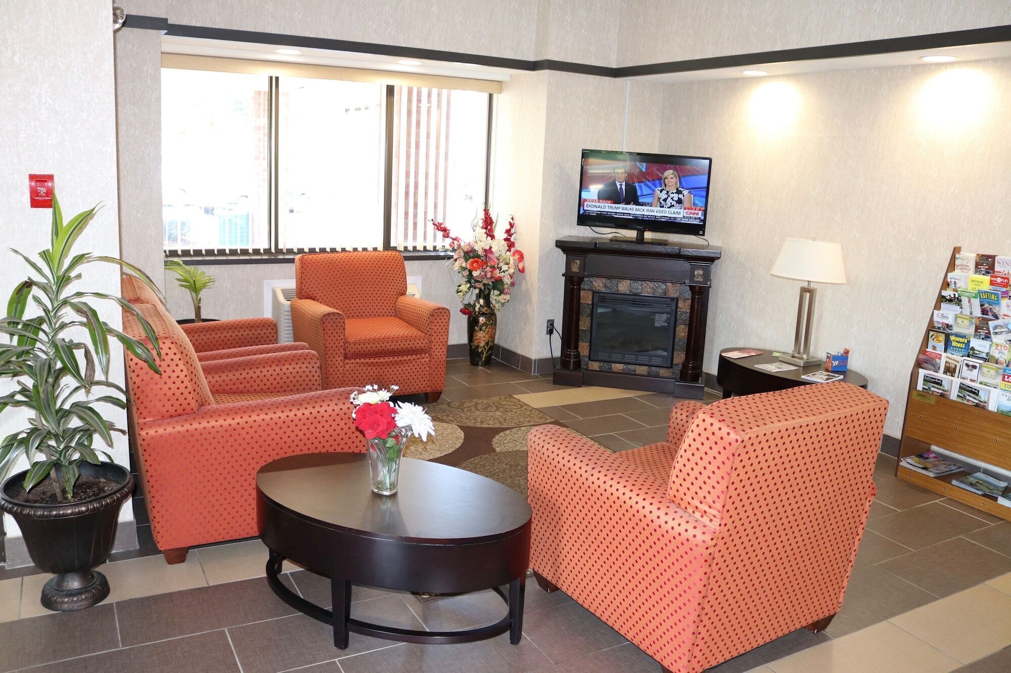 Een hotel lobby met een open haard, zithoek, televisie en een kleine tafel met een bloevas.