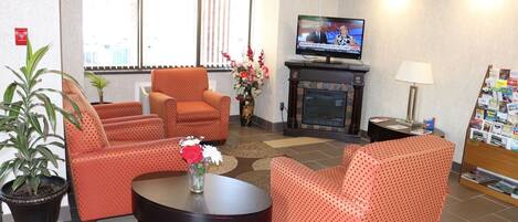 A hotel lobby with a fireplace, seating area, television, and a small table with a vase of flowers.