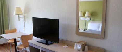 Camera d'albergo con una scrivania, una TV a schermo piatto, uno specchio, una lampada e una tenda verde.