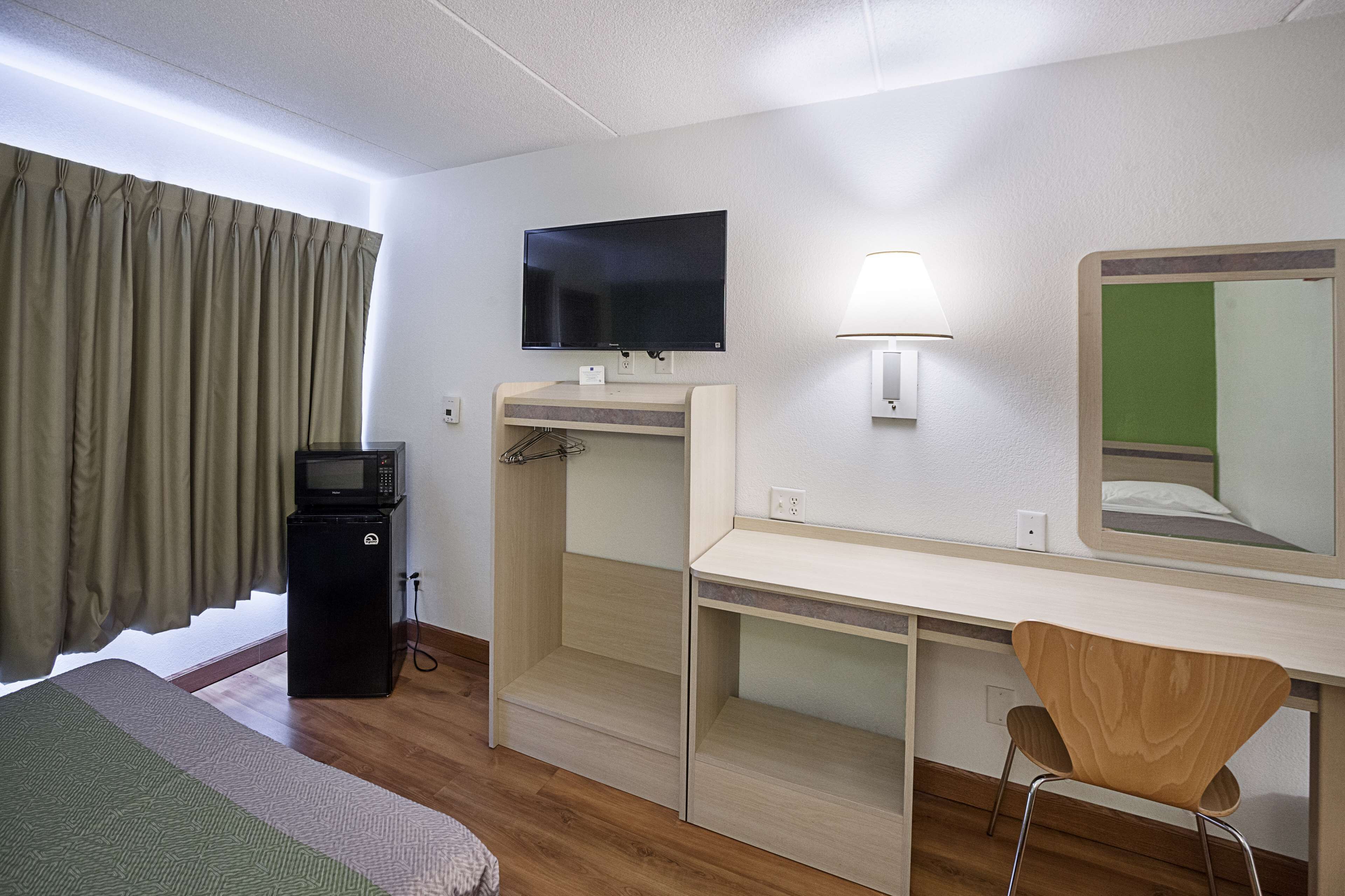 Een hotelkamer met een bed, een bureau met stoel, een televisie, een lamp en een magnetron.