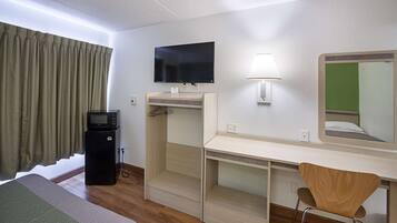 Een hotelkamer met een bed, een bureau met stoel, een televisie, een lamp en een magnetron.