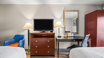 Habitación de hotel con una cama, un escritorio con televisor, dos lámparas, una silla, armario y espejo.
