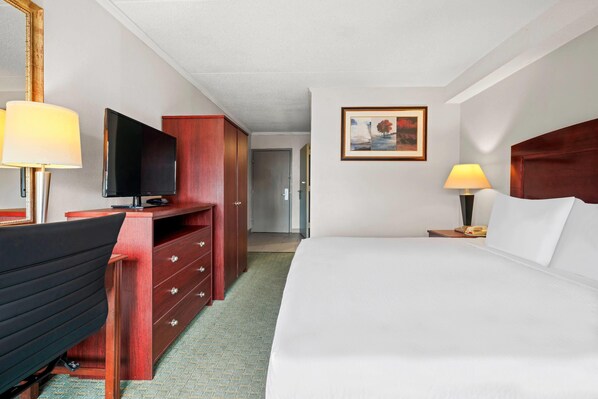 Habitación de hotel con cama, escritorio con silla, televisor, cómoda y un cuadro en la pared.