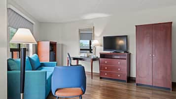 A modern hotel room with a blue sofa, a wooden desk, a television, and a wardrobe.