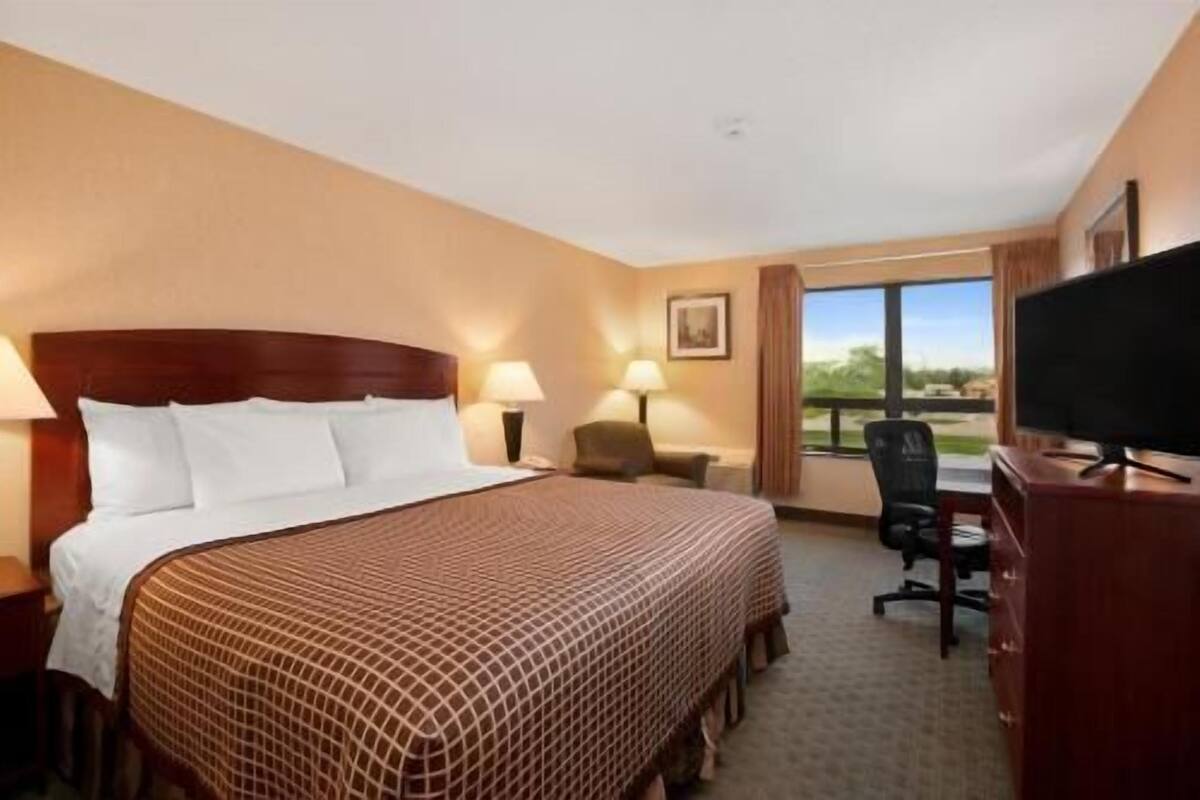 Une chambre d’hôtel avec un grand lit, un bureau avec une chaise, une télévision et une fenêtre donnant sur un beau paysage.