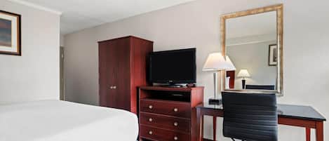 A hotel room with a bed, a wooden dresser with a television, a desk with a chair, and a large mirror on the wall.