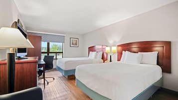 A hotel room with two beds, a desk with a computer, a chair, and a lamp.
