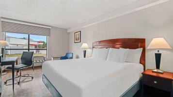 A hotel room with a large bed, a desk with a chair, two bedside lamps, and a window with a view of a building.