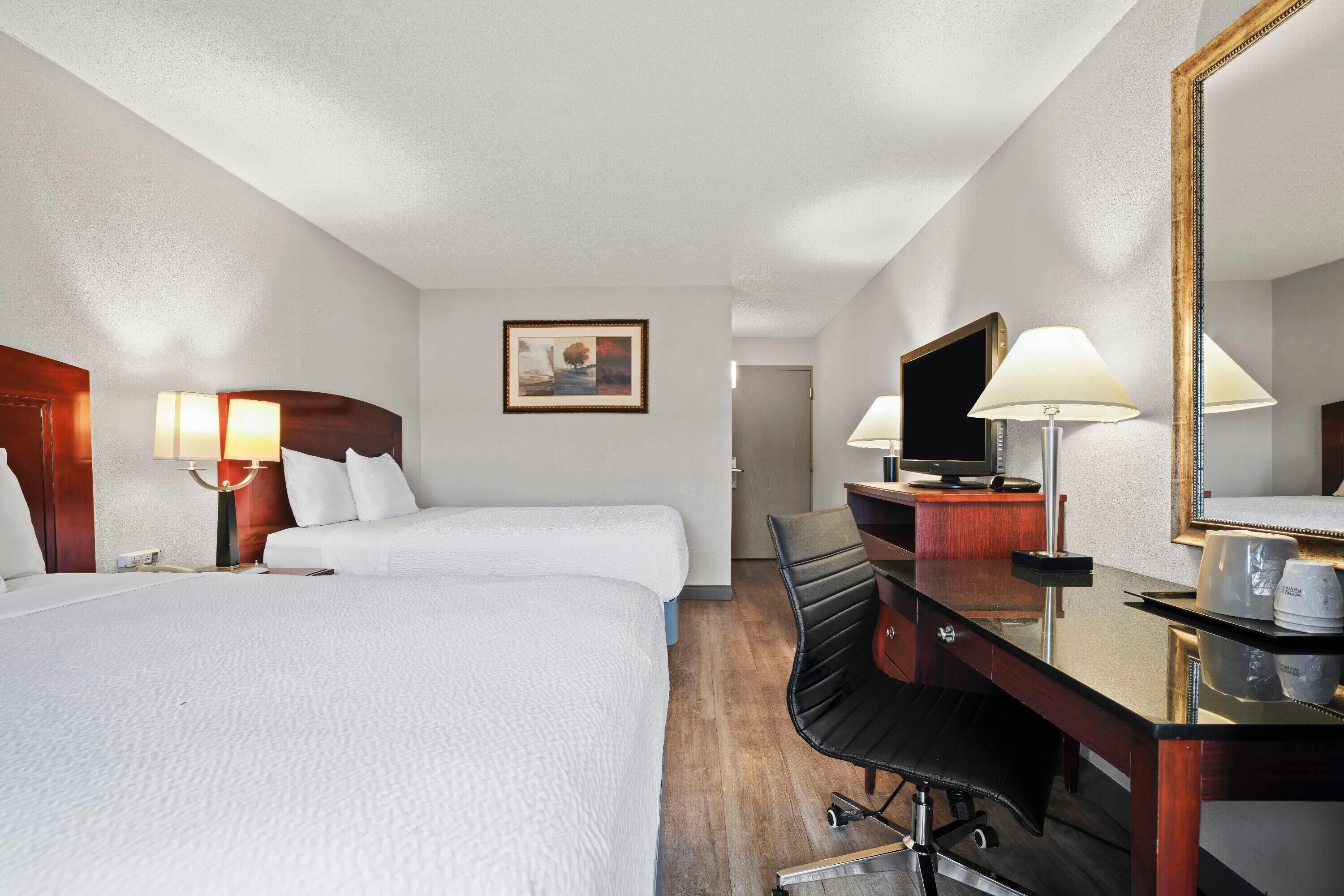A hotel room with two beds, a desk with a chair, a television, and a mirror.