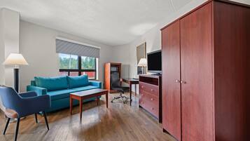 A room with a blue sofa, a wooden desk, a red wardrobe, and a television.