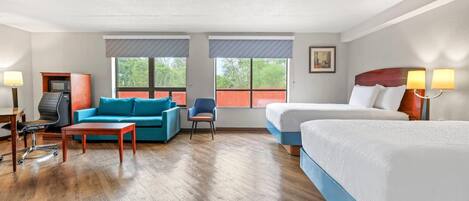 Una habitación de hotel con dos camas, un sofá, un escritorio, una silla y un televisor.